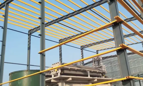 Yellow FRP beams installed as purlins on a gray steel frame at an industrial construction site.