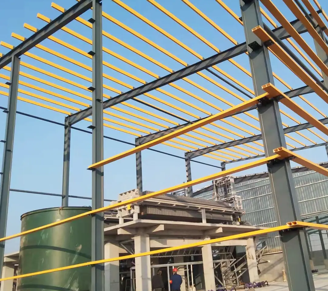 Yellow FRP beams installed as purlins on a gray steel frame at an industrial construction site.